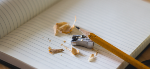 Pencil, pencil sharepener, and pencil shavings on top of a open notebook