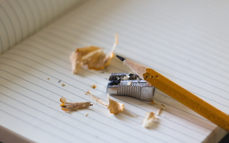 Pencil, pencil sharepener, and pencil shavings on top of a open notebook